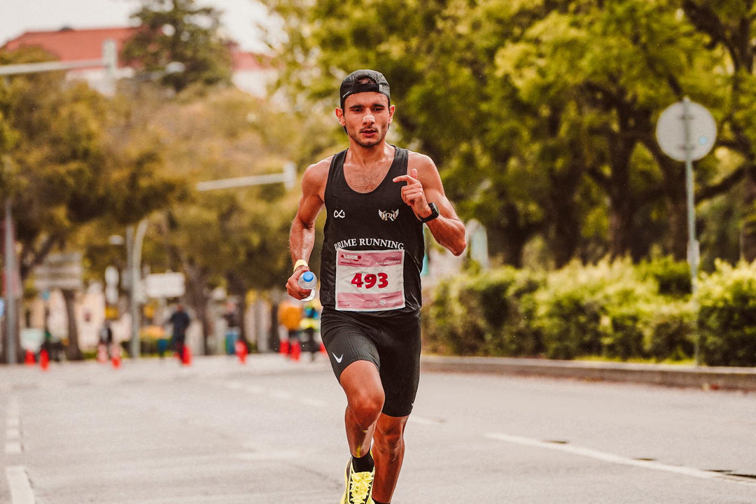 Focused male athlete running in a marathon, wearing a tank top and holding a bottle of water.