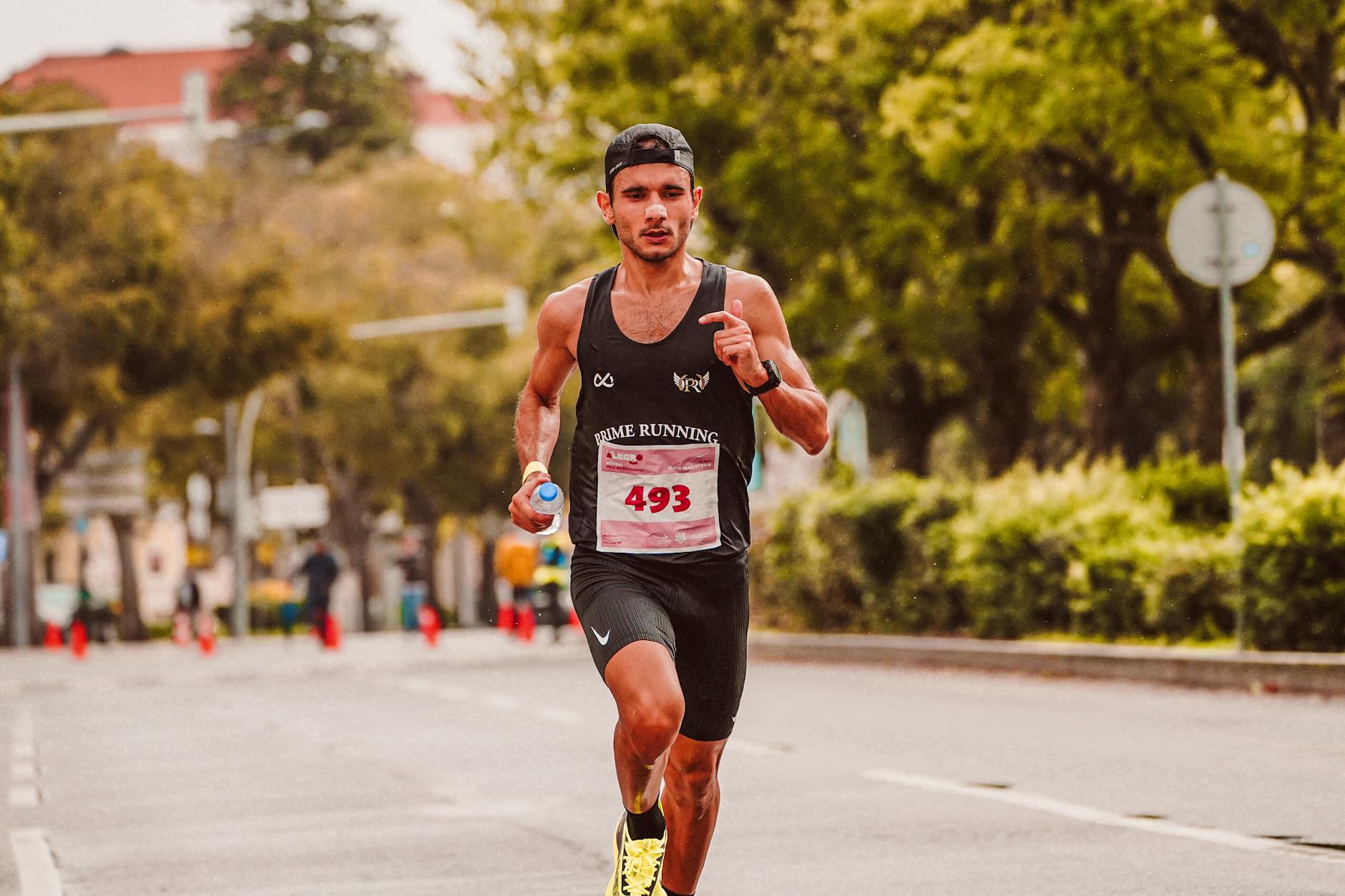 Focused male athlete running in a marathon, wearing a tank top and holding a bottle of water.