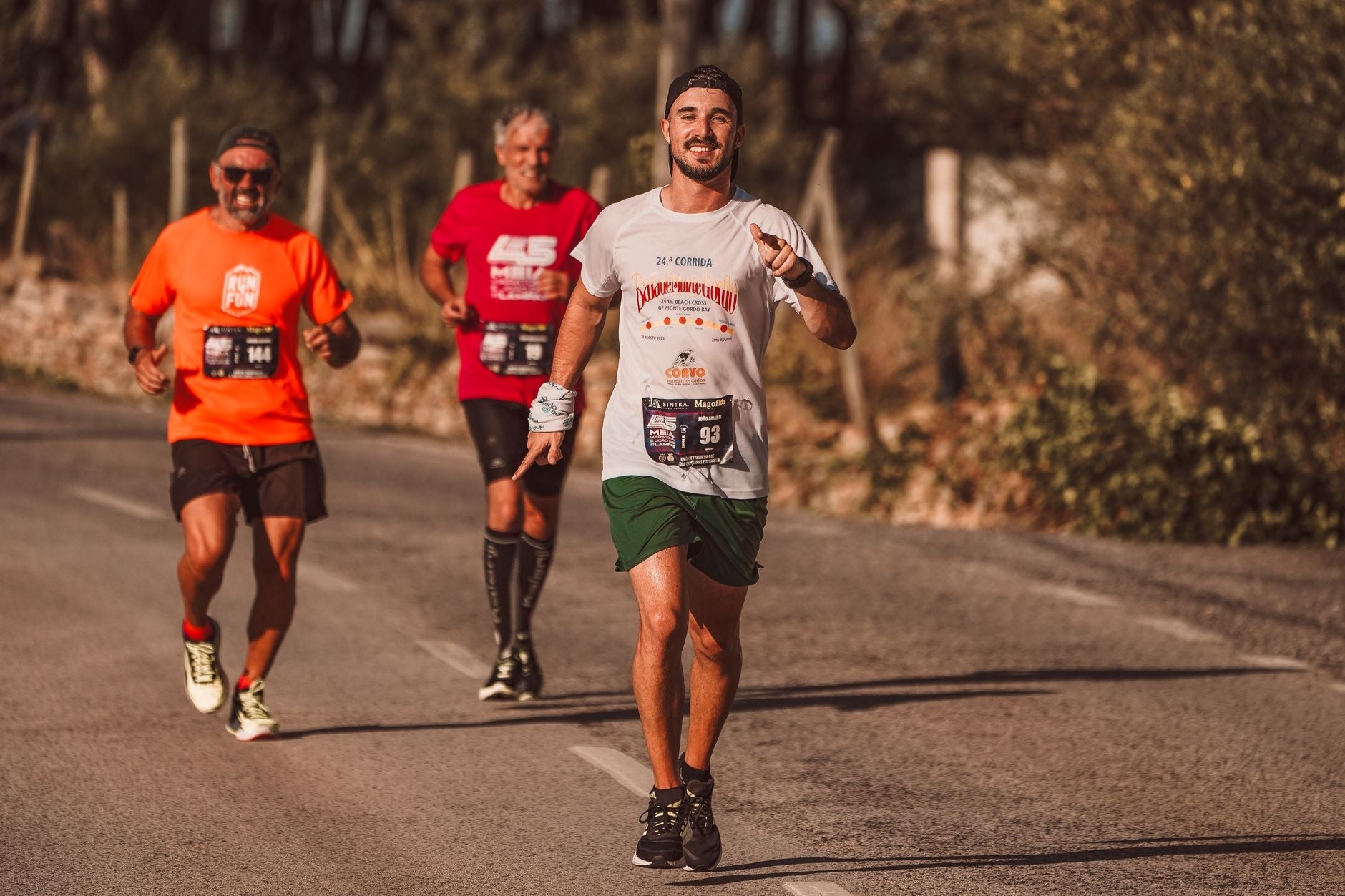 Three men running in a sunny road race during summer training