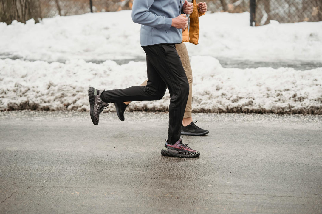 Side view of joggers running together on a road in a snowy park during cold winter training