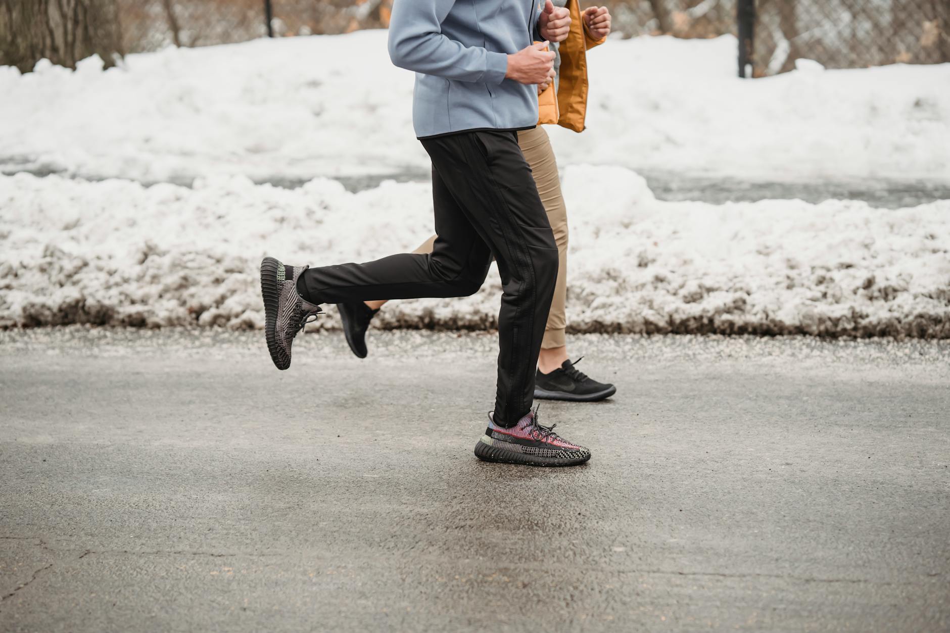 Side view of joggers running together on a road in a snowy park during cold winter training